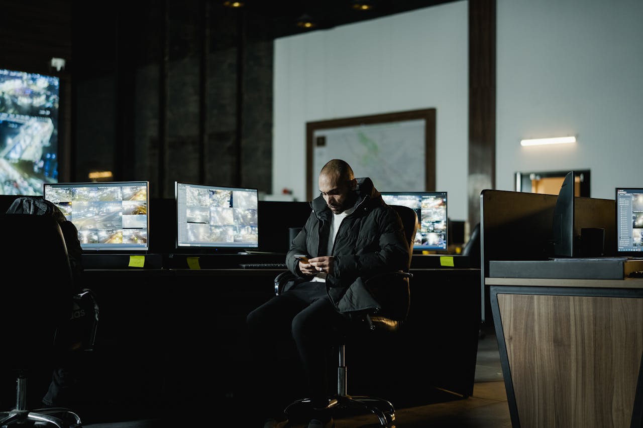 hero-img-01 Security officer seated in a dimly lit control room, analyzing multiple surveillance screens.